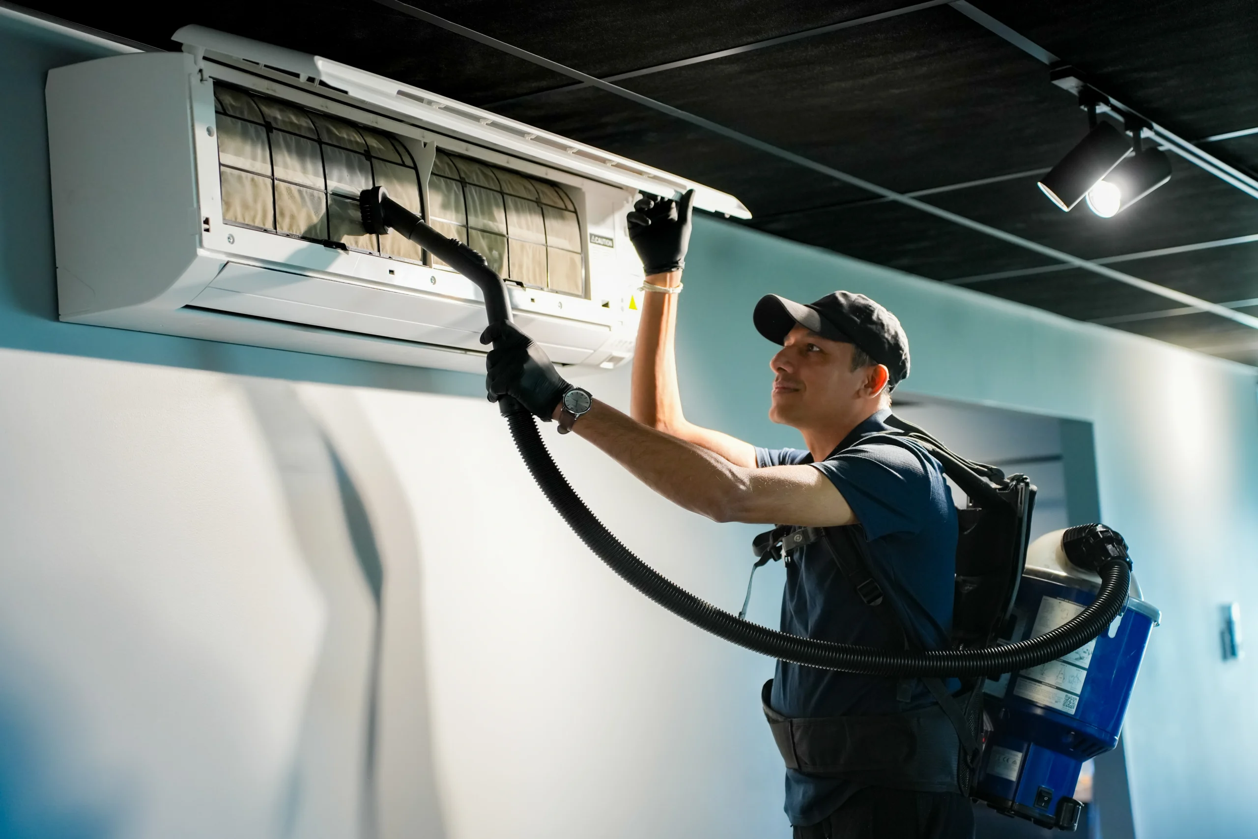 A cleaner from Hobart Cleaning Company vacuuming the filters of an air conditioner, showcasing detailed commercial office cleaning and maintenance services.