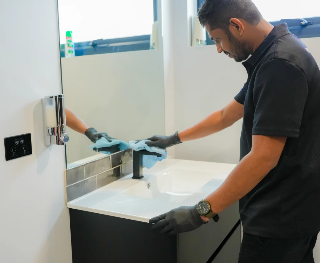 A cleaner from Hobart Cleaning Company detailing a bathroom sink, showcasing thorough domestic and commercial washroom sanitization services in Hobart.